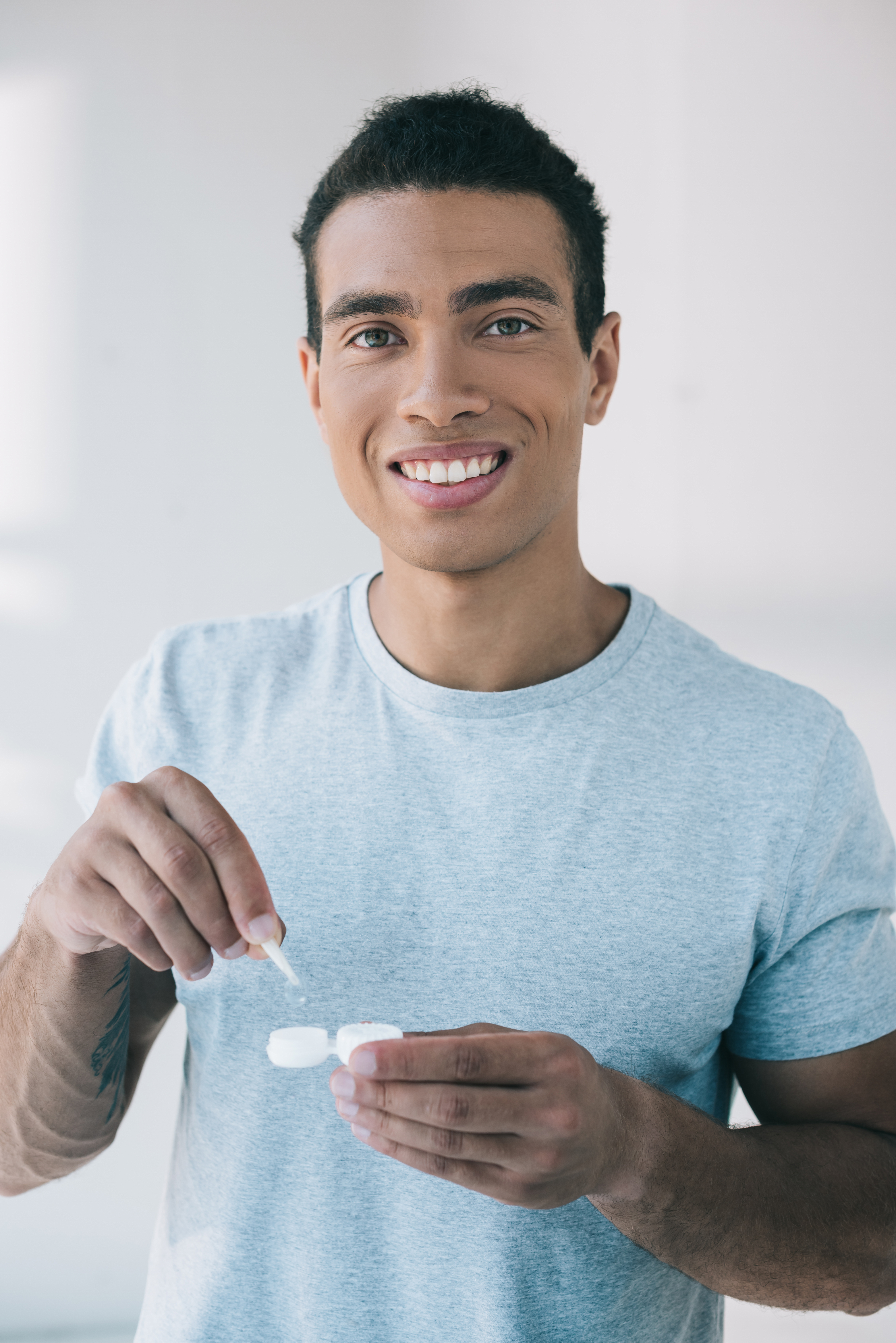 handsome man taking contact lens with tweezer from container while looking at camera